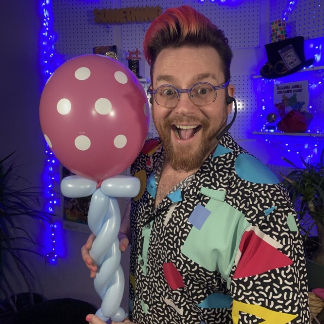 Dave Brenn holding a pink polka dot balloon sculpture with a big smile during a balloon entertainment show.