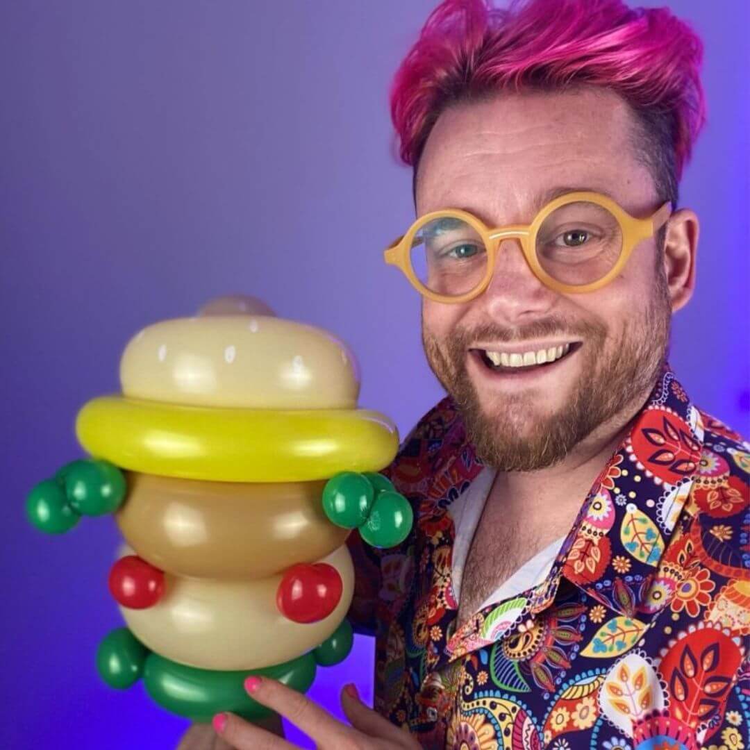 Dave Brenn holding balloon sculpture resembling stacked burger