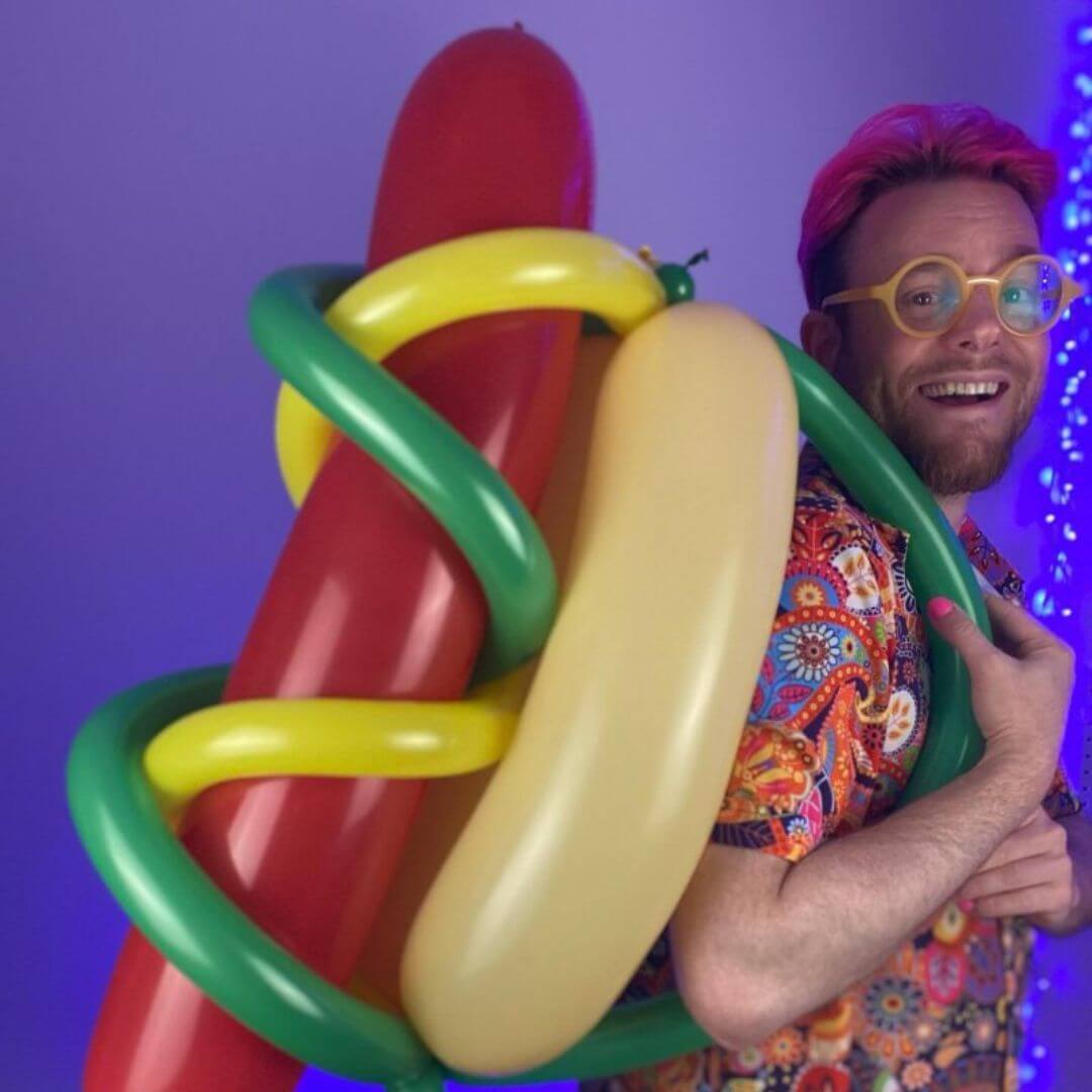 Dave Brenn wearing giant hotdog balloon sculpture and smiling